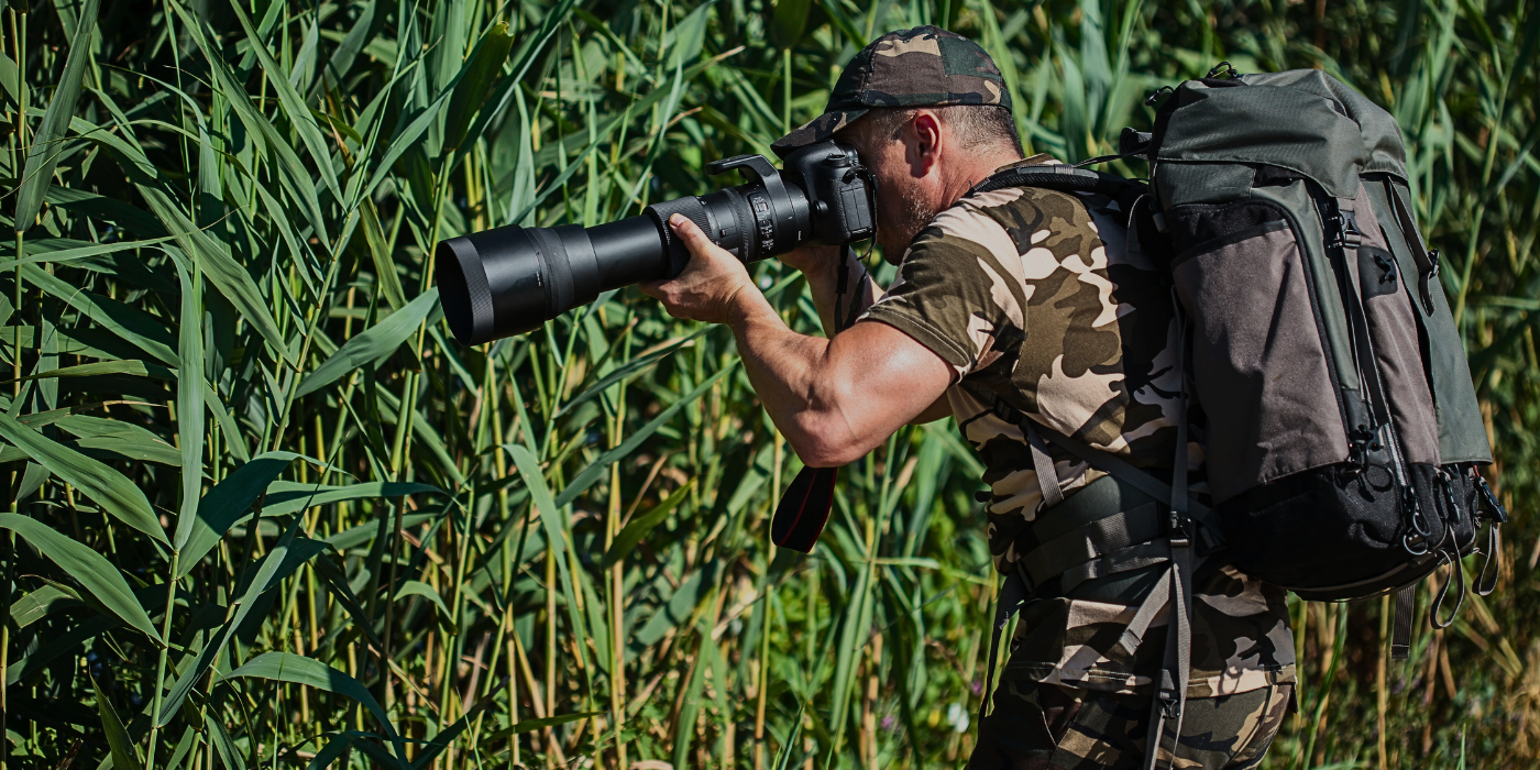 Wildlife photographer in camouflage gear using a telephoto lens in the Kinabatangan Rainforest, Sabah, Borneo, during a nature photography expedition