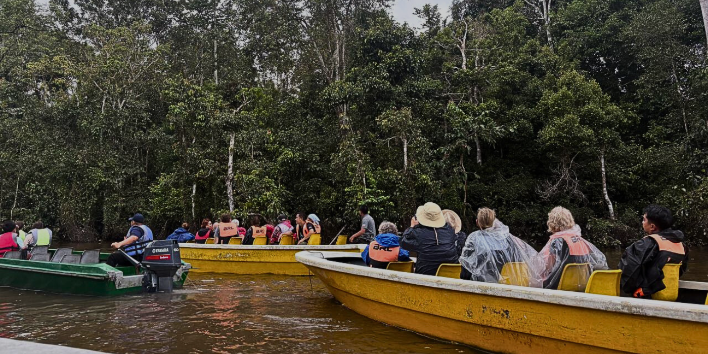 Tourists on a Kinabatangan River safari cruise searching for wildlife in Borneo's rainforest.
