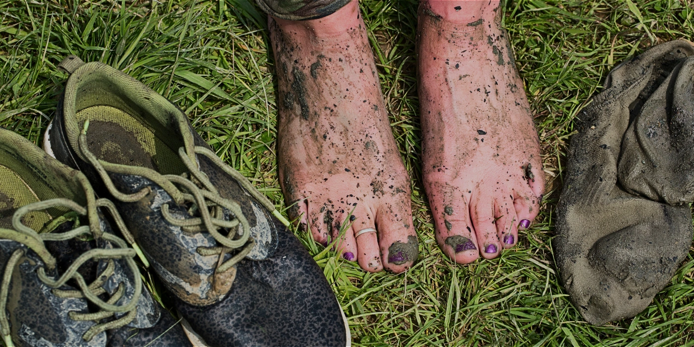 Close-up of heavily mud-covered hiking shoes resting on the forest ground after a challenging jungle trek on Gunung Tahan in Taman Negara