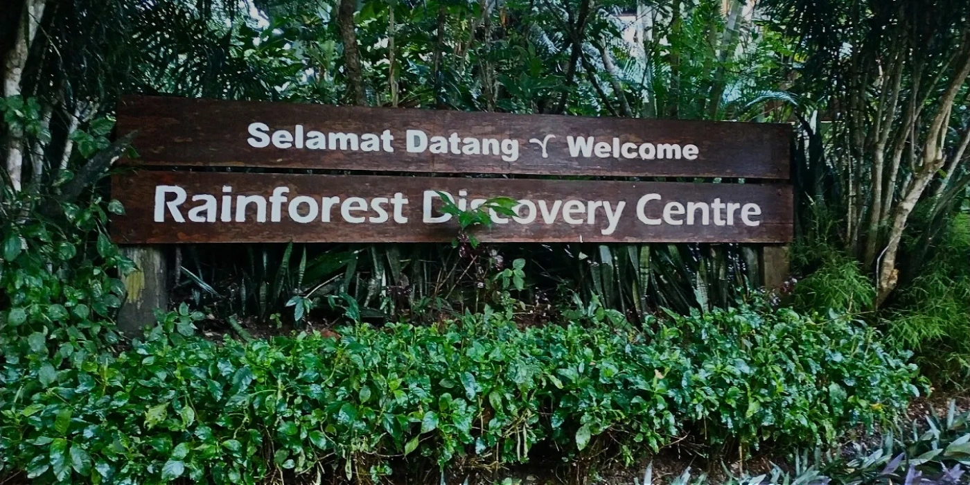 Entrance signage of the Rainforest Discovery Centre in Sepilok, Sabah, surrounded by lush greenery and tropical rainforest plants.
