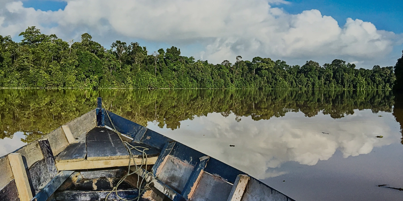 Tour boat cruising along Kinabatangan River under bright daylight, surrounded by Borneo rainforest