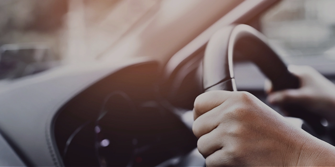 Close-up of a person’s hands on a car steering wheel during a road trip to Sandakan, Sabah