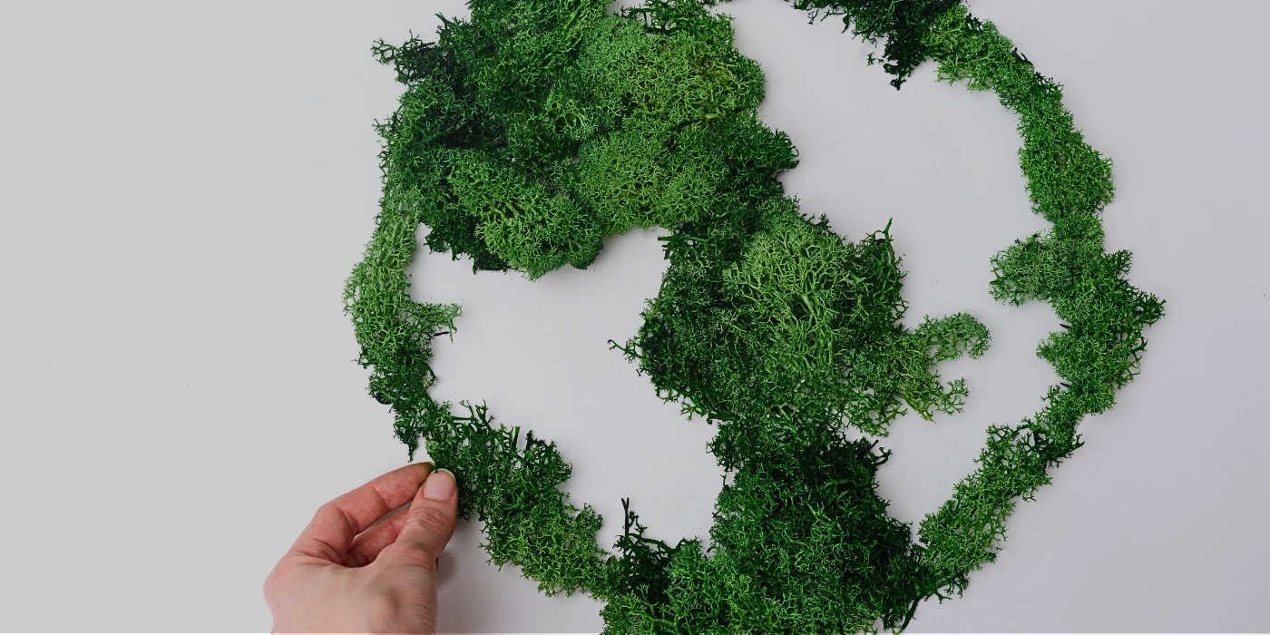 A person shaping a globe made of green leaves, symbolizing sustainable and eco-friendly travel- sustainable travel in kinabatangan