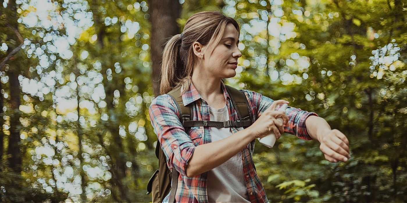 Woman applying insect repellent spray on her arms in a tropical rainforest environment