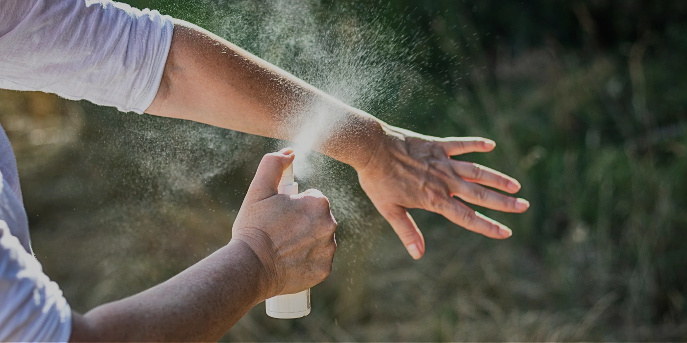 a person spraying insect repellent on his arm.